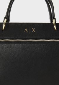 Sac à main en cuir noir avec une surface texturée, quincaillerie dorée, fermeture éclair sur le dessus et initiales embossées "A | X" à l'avant.