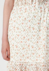 Robe florale blanche ornée de petites fleurs roses et vertes, en tissu texturé, avec un ourlet volanté. Comprend une taille élastique pour un ajustement parfait.