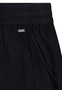 Pantalon en tissu noir texturé avec taille élastique, poche latérale et petite étiquette métallique rectangulaire de la marque près de la taille.