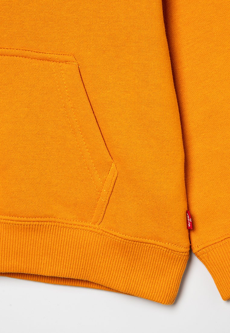 Sweatshirt orange en coton doux, avec une poche kangourou, des manches et un ourlet côtelés, et une petite étiquette logo rouge sur le côté.