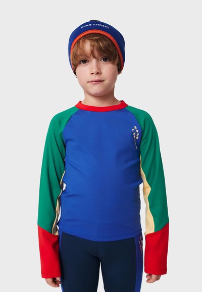 Rash guard a maniche lunghe colorato con corpo blu, maniche verdi e rosse, e dettagli gialli; materiale morbido e elastico; include dettaglio del logo.