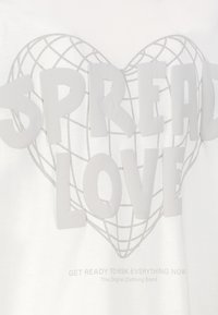 White t-shirt featuring raised gray text "SPREAD LOVE" over a heart-shaped grid design. Below, smaller text reads "GET READY TO RISK EVERYTHING NOW."