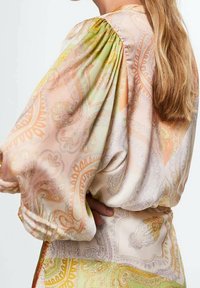 Blusa de manga larga en tejido ligero y sedoso con un estampado de paisley en tonos pastel de naranja, verde y beige. Mangas abullonadas fruncidas.