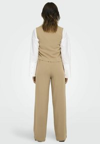 Beige skræddersyet vest med lav ryg, parret med vide bukser. Materialet ser glat ud, med en struktureret design og rene linjer.
