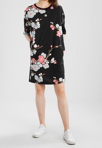 Svart klänning med blommönster i rosa, grått och vitt, korta ärmar och en lös passform, i kombination med vita sneakers.