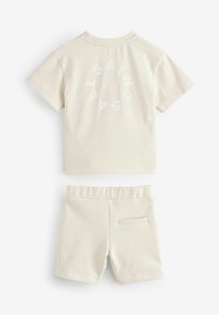 Beige bomulds skjorte med korte ærmer og cirkulært hvidt "SAINT" tryk samt matchende shorts med elastisk talje og baglomme.
