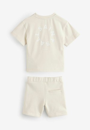 Beige katoenen shirt met korte mouwen met een ronde witte "SAINT" print en bijpassende shorts met een elastische tailleband en een achterzak.