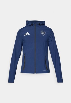 Marineblau wetterfeste Jacke mit Frontreißverschluss, Kapuze, Adidas-Logo, Arsenal-Wappen und schwarzen Reißverschlusstaschen. Leichter Stoff, glatte Textur.