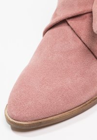 Bottine en suede rose à bout pointu, avec une texture lisse et un accent cousu le long du devant. Semelle en bois plate.