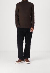 Pull à col roulé côtelé marron, pantalon large noir, et baskets marron à semelles blanches. Design simple, texturé, et couleurs neutres.