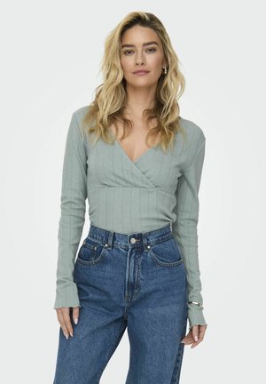Lichtgroene lange mouwen wikkeltop met verticale ribbels en een V-hals, gecombineerd met hoog-waist blauwe denim jeans met een knoopsluiting.