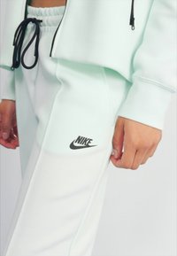 Licht mintgroene Nike sweats met een trekkoord in de taille en zwart logo op de linker bovenbeen, met een gladde, zachte textuur.