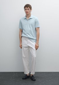 Light blue short-sleeve polo, white tailored trousers, black loafers. Smooth fabric, fitted silhouette, minimalistic design. Plain backdrop.