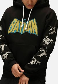 Felpa nera con cappuccio caratterizzata da un grande logo "BATMAN" giallo e blu sulla parte anteriore e illustrazioni bianche di Batman sulle maniche. Materiale in cotone.