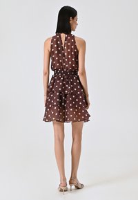 Braunes Kleid mit Punkten, Halterneck, geschichtetem Rüschendesign, elastischem Taillenbund und transparentem Stoff. Der Rücken hat ein Schlüssellochdetail.
