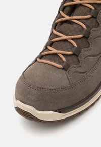 Brown suede hiking shoe with textured fabric upper, beige accents, and brown laces. Contoured shape with stitched detailing and rubber outsole.