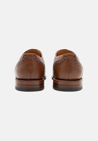 Chaussures en cuir marron avec une finition texturée, bout arrondi et détails de broguing décoratifs. Talon en bois massif avec base noire.