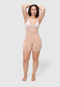 Beżowy bezszwowy modelujący body z dekoltem w kształcie litery V i regulowanymi ramiączkami, o dopasowanym kroju sięgającym do połowy uda. Gładka faktura.