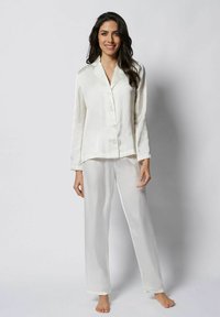 Set de pijama din mătase în crem deschis; include mâneci lungi, închidere cu nasturi și pantaloni drepți cu o textură fină. Design elegant.