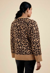 Pull en imprimé léopard dans des tons de beige et noir, avec un col et un ourlet côtelés, une coupe décontractée et un matériau en tricot texturé.
