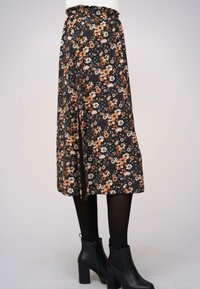 Fustă midi florală, de culoare neagră, cu flori portocalii, crem și albastre. Dispune de un talie elastică și o fanta pe lateral. Este purtată cu cizme negre până la gleznă.