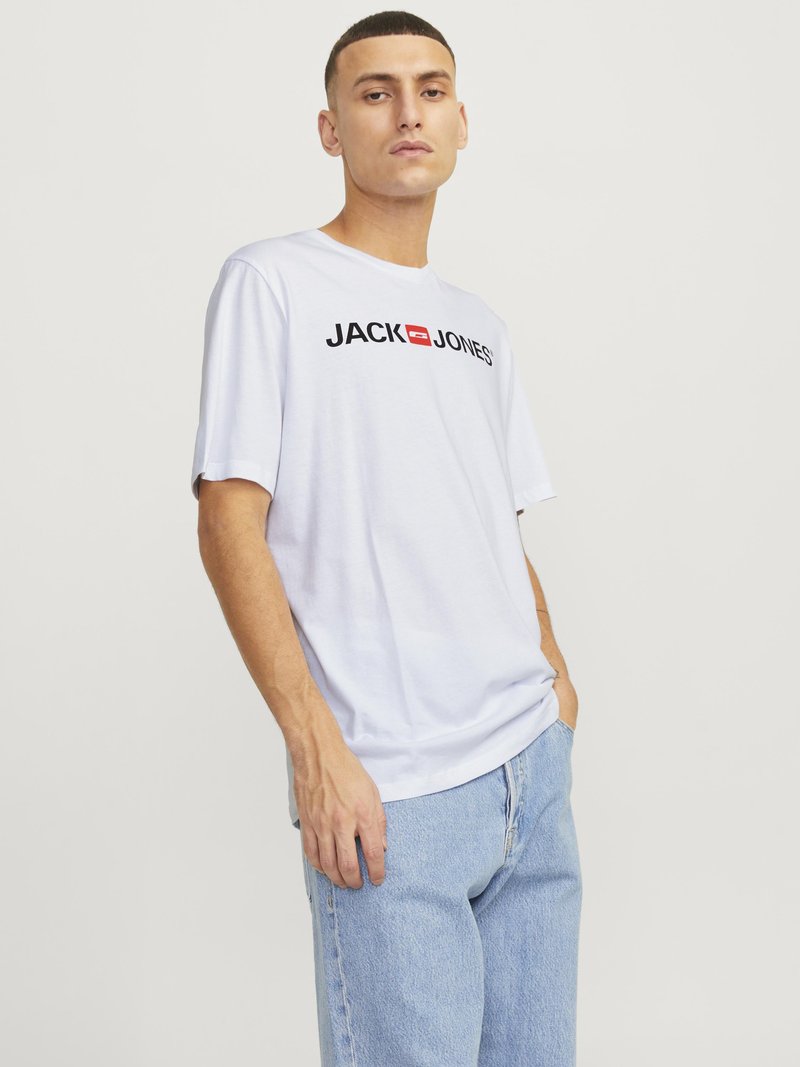 Balta medvilninė marškinėliai trumpomis rankovėmis su mustruotu juodu "JACK & JONES" logotipu centre ant krūtinės, derinami su šviesiai mėlynomis džinsomis.