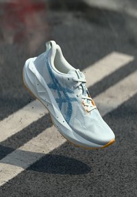 Lightweight running shoe in white with blue accents. Mesh upper for breathability, textured sole, and orange outsole for grip.