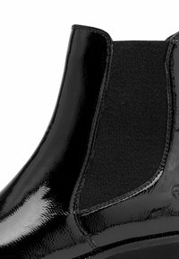 Černá lakovaná kotníková bota s elastickými postranními panely. Hladký, lesklý povrch, zaoblená špička a gumová podrážka s minimálním vzorem protiskluzu.