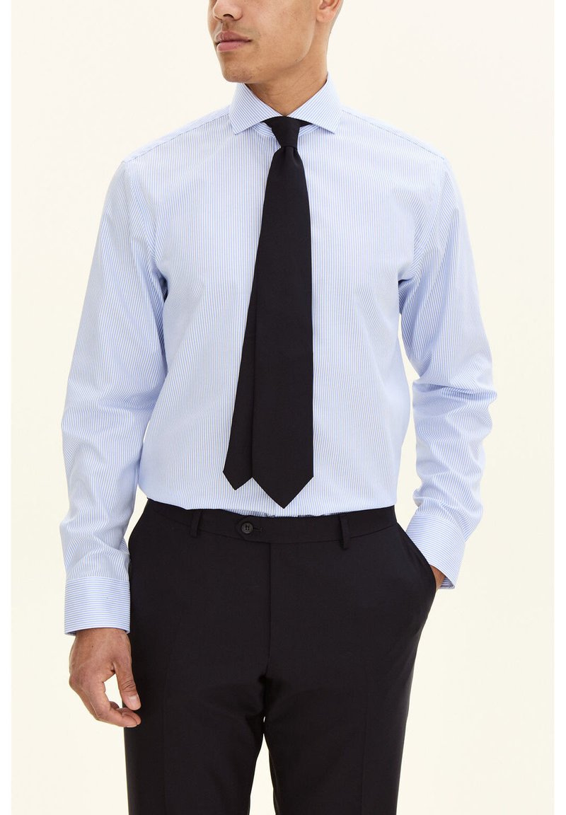 Vaaleansininen raidallinen kauluspaita, jossa on napillinen kaulus, pitkät hihat ja musta solmio, yhdistetty tummiin housuihin. Pehmeä kangaspinta.