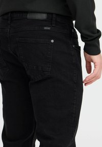 Svarta jeans i denim med klassisk passform, med en texturerad yta, två bakfickor och en liten logotyp på midjebandet.