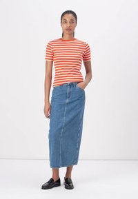 Rød og hvit stripete kortermet t-skjorte parret med et langt blått denimskjørt. Modellen har på seg svarte sko. Hvit bakgrunn.