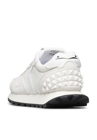 Sneaker bianco realizzato in materiali scamosciati e in pelle, con una parte posteriore testurizzata arricchita da borchie a piramide e una suola in gomma nera.