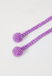 Purple beaded string with two pom-pom ends. The beads are small and smooth, creating a textured surface and a continuous design.