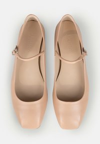 Pereche de pantofi Mary Jane bej din piele, cu vârfuri pătrate și curele ajustabile cu cataramă, văzuți dintr-o parte pe fundal alb.