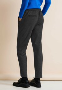 Pantaloni jogger neri a gamba affusolata con una finitura testurizzata, dotati di una vita elasticizzata e tasche laterali, abbinati a scarpe nere con lacci.