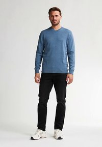 Světle modrý svetr s výstřihem do V a dlouhými rukávy, spárovaný s černými džíny a bílými sportovními botami. Hladká textura a přiléhavý střih.