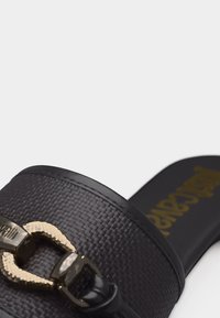 Μαύρο σαγιονάρι με υφή και λεπτομέρεια χρυσής αλυσίδας από μέταλλο στην κορυφή και λείο μαύρο πέλμα.