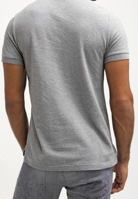 Harmaa puuvillainen t-paita, jossa on lyhyet hihat ja klassinen leikkaus. Sileä pinta, minimaaliset saumat, resoroitu kaula-aukko. Ei näkyvää brändäystä tai kuvioita.