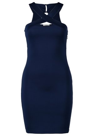 Femme portant une robe sans manches bleu marine avec des bretelles croisées, des collants noirs transparents, des talons noirs et de longues boucles d'oreilles argentées à franges.