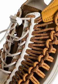 Baskets marron et crème avec un design de lacets tressés, des réglages élastiques et des accents en suède. Matériaux texturés avec un motif en boucle unique.