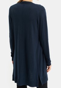 Marinblå lång cardigan med ribbade manschetter och nederkant, ventilerade sidor, tillverkad av mjukt tyg, med en slät yta och minimalisk design.