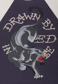 Camiseta púrpura con un gráfico de una pantera negra rugiente y el texto "DIBUJADO POR" en beige. La tela es suave con un corte clásico.