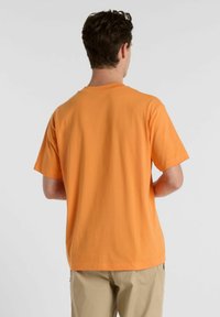 Short-sleeve, crew-neck t-shirt in bright orange cotton with a smooth texture, shown from the back, paired with beige pants.