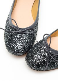 Des ballerines noires et argentées pailletées présentent un bout arrondi, un liseré en tissu gris lisse et un nœud assorti sur chaque bout.