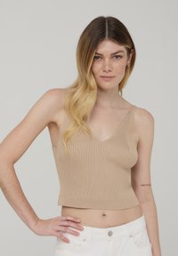 Top corto a costine beige con scollo a V e spalline sottili, realizzato in un materiale morbido. Presenta una silhouette aderente.