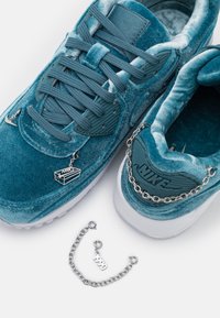 Snabba i teal sammet har texturerade överlagringar, matchande snören och silverkedjeaccent. Inkluderar charm och två dekorativa metallbitar.