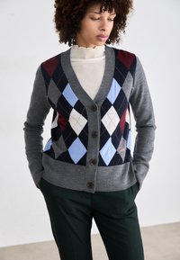 Grå cardigan med V-hals, med et flerfarget argyle-mønster i burgunder, lyseblå, marineblå og hvit. Fem mørke knapper foran.