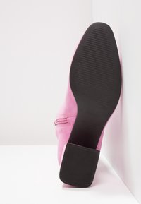 Rosa mocka ankelstövlar med svart gummisula, med en sidodragkedja och en fyrkantig klack, visade bakifrån.