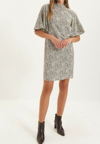 Vestido de manga corta en un beige claro con un patrón salpicado en negro, fabricado con una tela suave y con un escote alto. Combinado con botas negras hasta los tobillos.