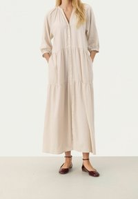 Robe en coton beige avec manches trois-quarts, devant boutonné, design à volants, poches latérales et coupe ample. Associée à des ballerines bordeaux.